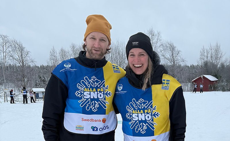 Två glada människor i Alla på snö-västar.